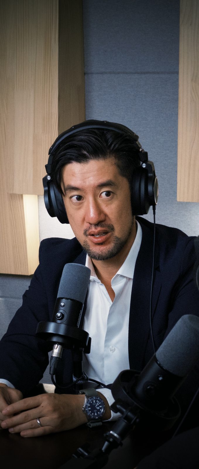 Tak Lo with studio headphones at the mic, turned toward Michael, recounting the 2003 Army deployment that landed him in Korea instead of Iraq